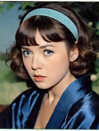 A brunette woman in 1950s fashion stands surprised amidst twilight orchard trees